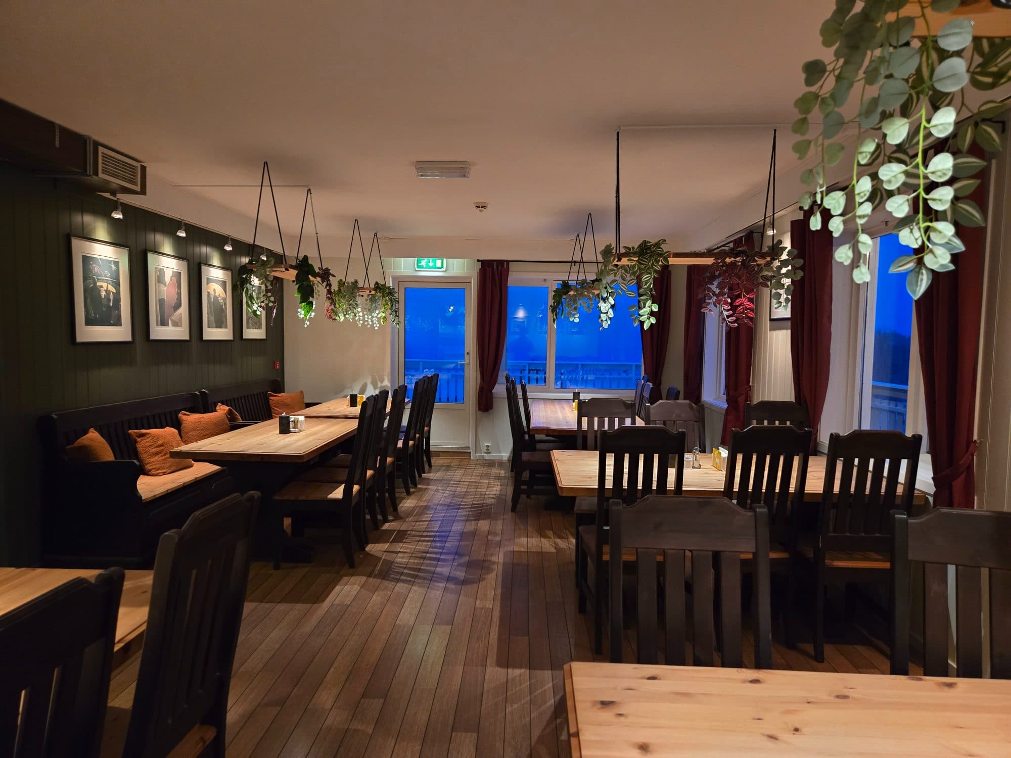 Restauranten med varmt treverk, planter og utsikt mot fjorden.